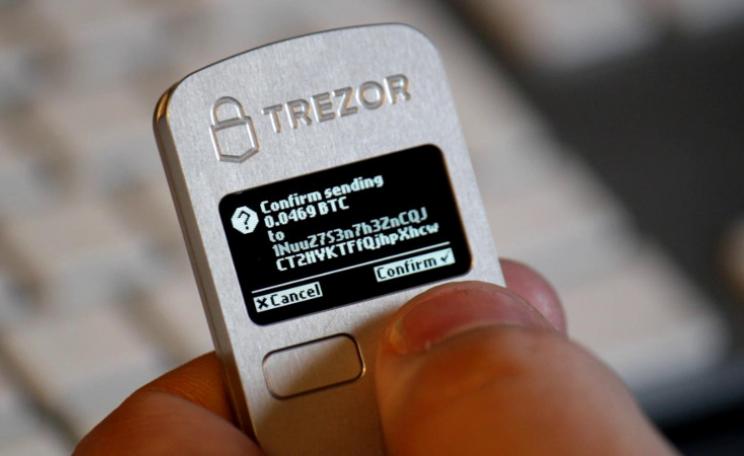 A TREZOR hardware wallet showing transaction details on its display.