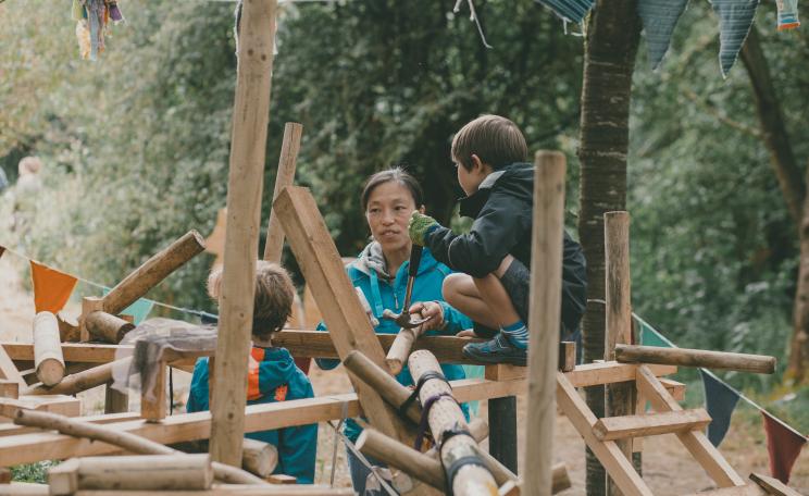 Children on a wooden playground structure that they are making themselves.