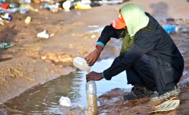 Deprived of piped water supply, a man in post-invasion Libya fills up a bottle of water from a muddy puddle. Photo: British Red Cross.
