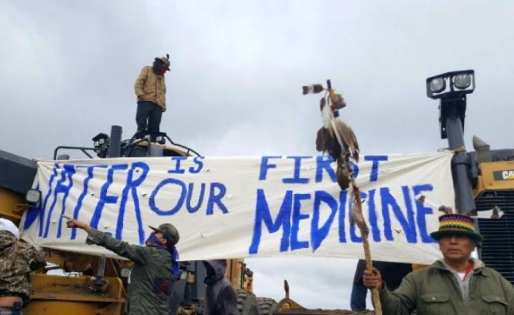 'Water is our first Medicine' - Water Protectors locked onto machinery, halting construction two days after the Dakota Access pipeline company bulldozed sacred burial sites. Photo: UnicornRiot.Ninja via Prachatai on Flickr (CC BY-NC-ND).