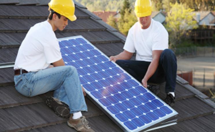 Workmen install a solar panel on a roof
